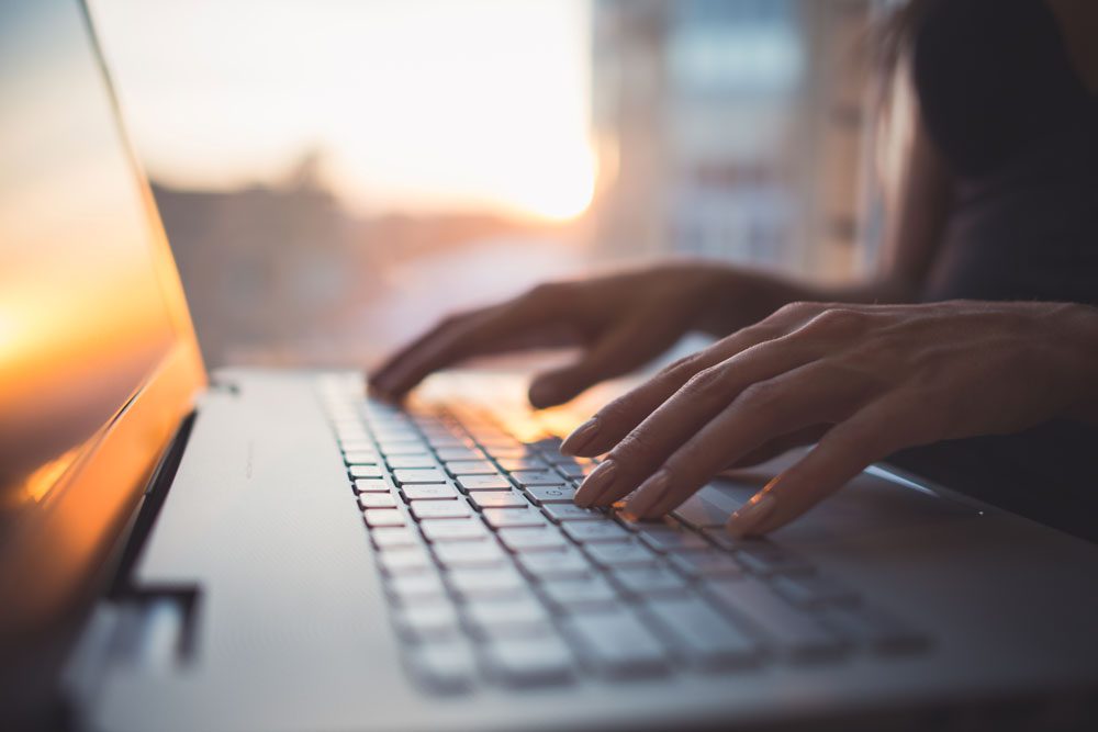 A person typing on a laptop with the sun shining.