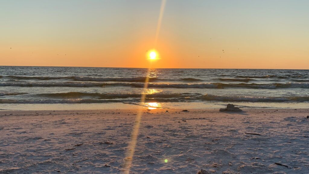 A sun setting over the ocean on a beach.