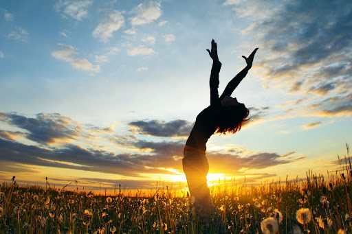 A woman standing in the grass with her arms up.